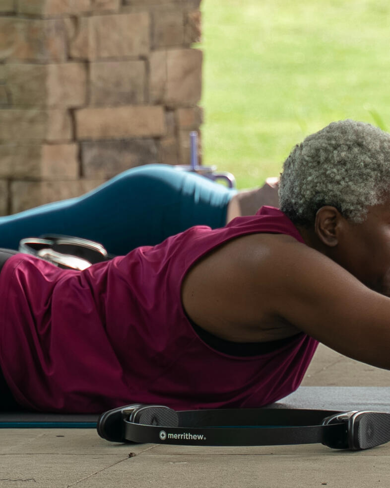 Participant performing back extension exercise on mat using Pilates ball during an outdoor Pilates class.