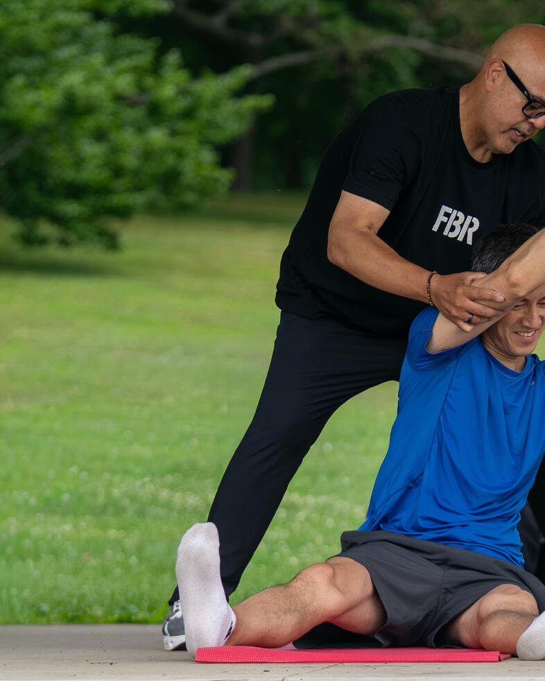 Rafael Jimenez assisting participant with an overhead side stretches using Pilates rings.